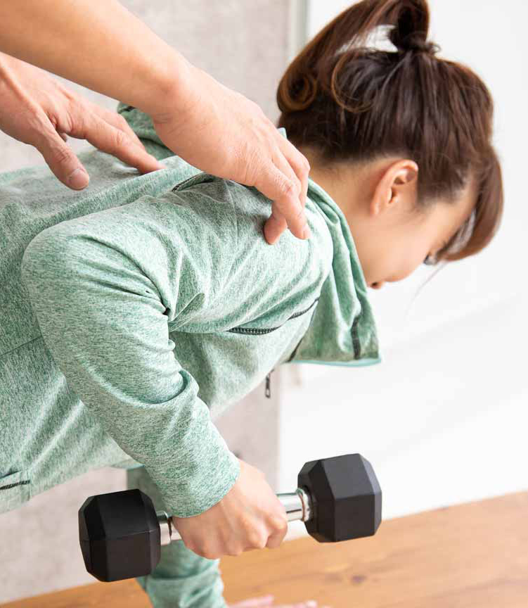 Personal trainer holding a woman's shoulder as she lifts weights